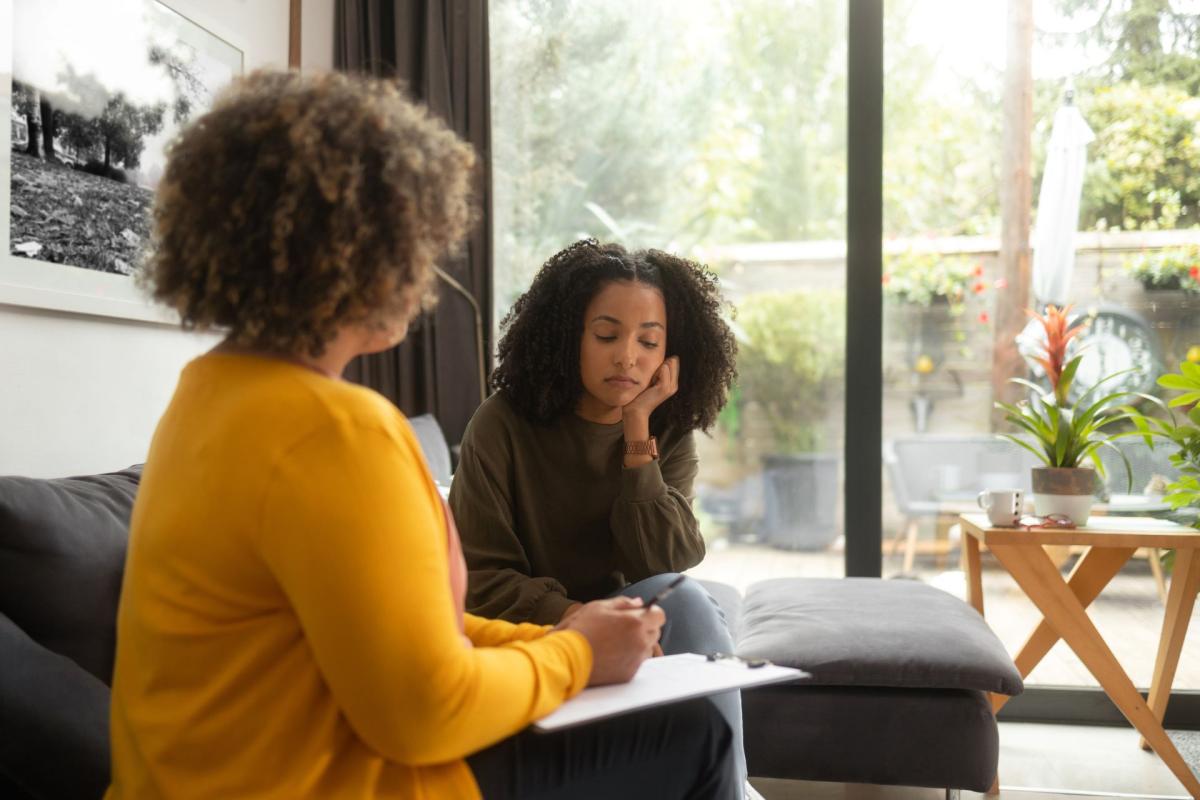 jeune femme assise sur un canapé et parle à une psychothérapeute dans un bureau / jonge vrouw zittend op een bank en praat met een psychotherapeut in een kantoor.