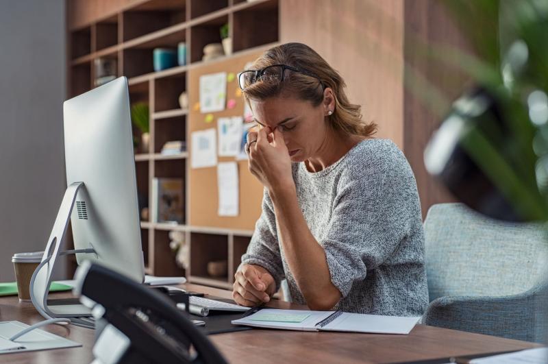 Femme travaillant face à un bureau et montrant des signes de fatigue / Vrouw werkt met uitzicht op een bureau en vertoont tekenen van vermoeidheid