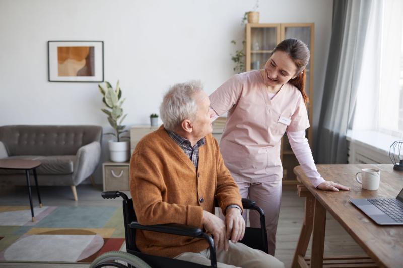 Soignante souriante échangeant avec une personne âgée en fauteuil roulant dans un intérieur chaleureux, illustrant les soins à domicile ou en institution. Soignante souriante échangeant avec une personne âgée en fauteuil roulant dans un intérieur chaleureux, illustrant les soins à domicile ou en institution.