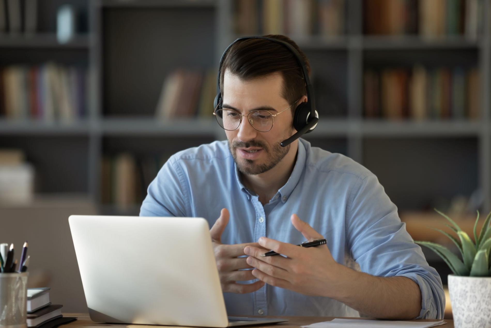 Conseiller santé portant un casque et assis à un bureau face à son ordinateur explique au patient quelles démarches entreprendre / Gezondheidsadviseur die een headset draagt en achter een bureau achter een computer zit en de patiënt uitlegt welke stappen hij moet nemen