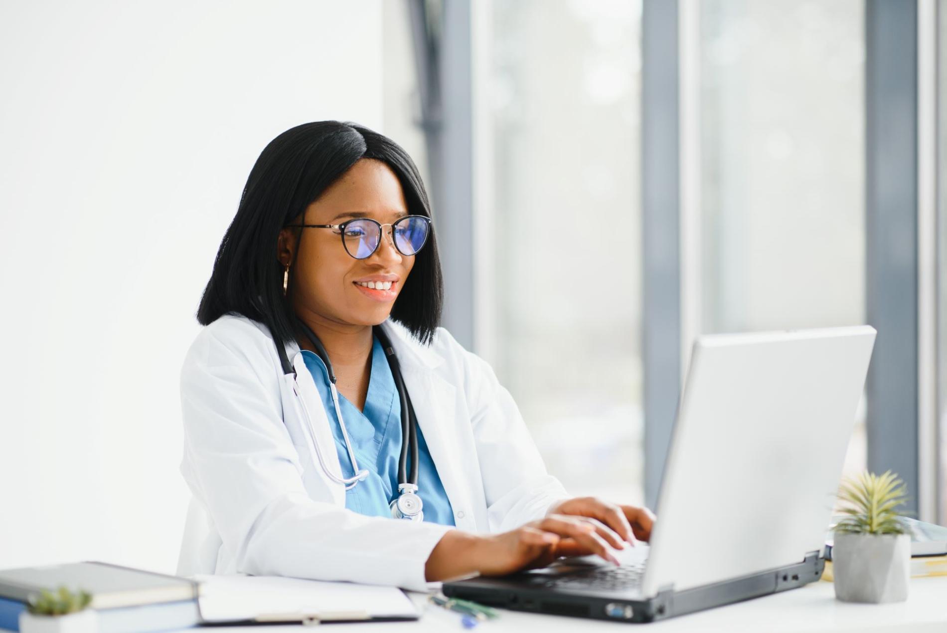 Portrait d'une jeune docteur afro-américain souriante qui encode des infos sur un ordinateur